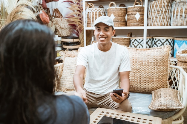 Craft entrepreneur and client make agreement by shaking hands when holding a smartphone in a craft gallery