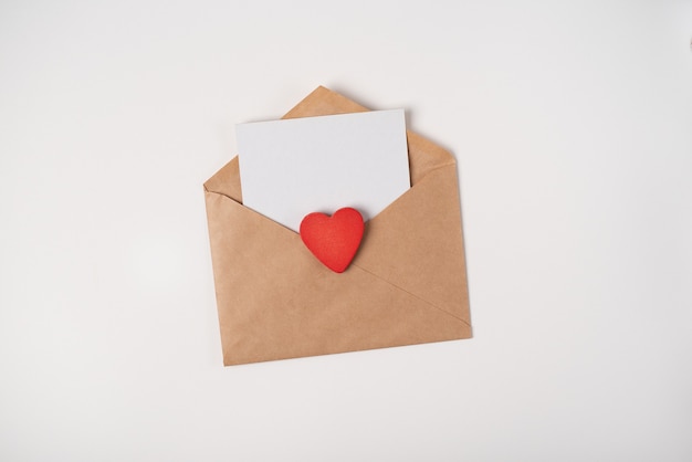 Craft envelope with a blank sheet inside and red wooden heart on the light (white) background.