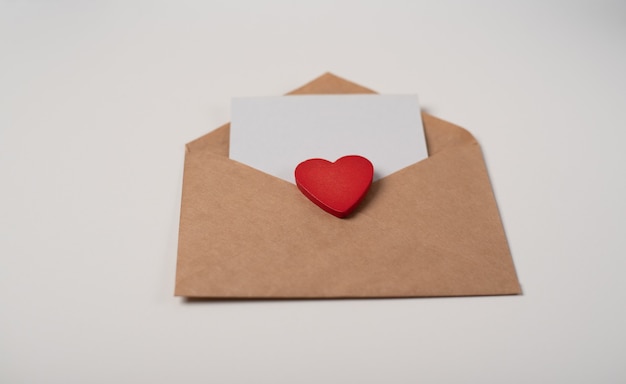 Craft envelope with a blank sheet of paper and a red heart on the white background. Romantic love letter for Valentine's day concept.