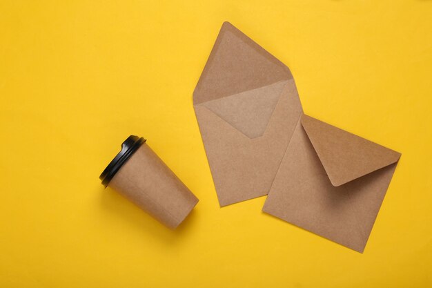 Craft envelopes and coffee cup on yellow background Top view