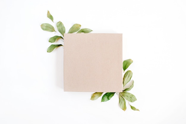 Craft gift box and floral composition with green leaves on white surface