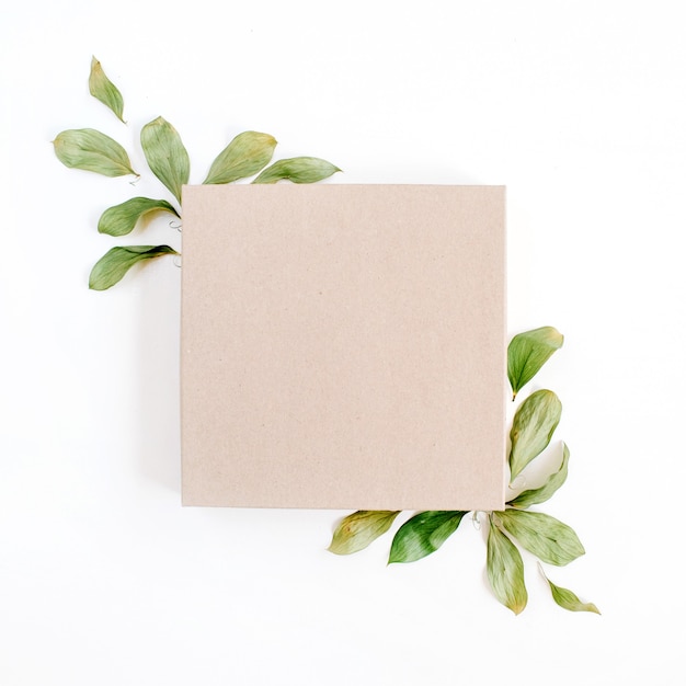 Craft gift box and floral composition with green leaves on white surface