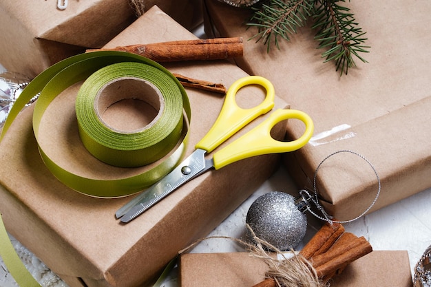 Craft paper with green ribbon and scissors making bow at xmas gift box decorated with snowflake on w...