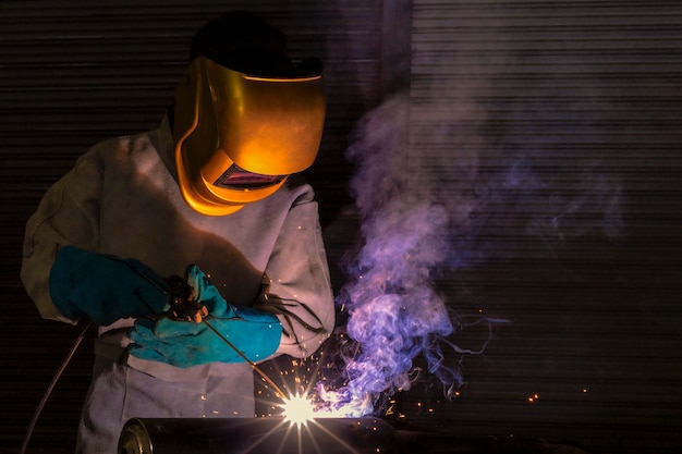 A craftman is welding with workpiece steel.Working person About welder steel Using electric welding machine There are lines of light coming out and safety equipment in factory industry.
