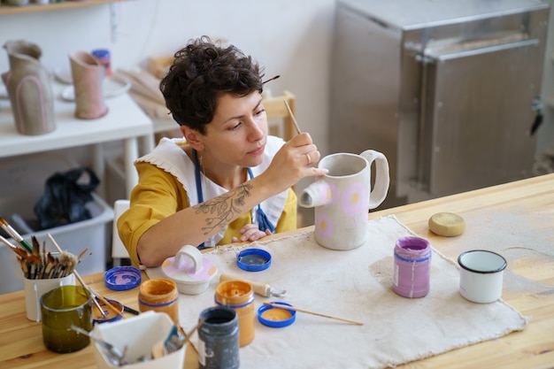 Crafts woman hold paintbrush decorating pottery jug at artistic classes in ceramic studio workshop