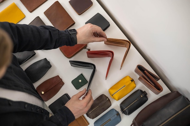 Craftsman hands laying out leatherwork on wooden showcase at leather workshop handwork accessories