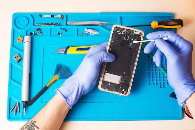 Craftsman in rubber gloves repair or service a mobile phone on a special rubber mat for repair view from the inside