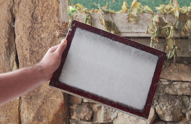 Craftsman's hands holding a wooden frame with vegetable fibers to make sheets of paper. Old traditional process of paper production.