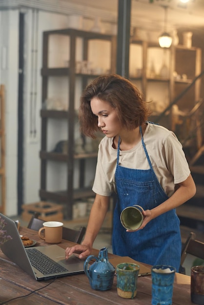 Craftswoman standing by table and looking at laptop screen