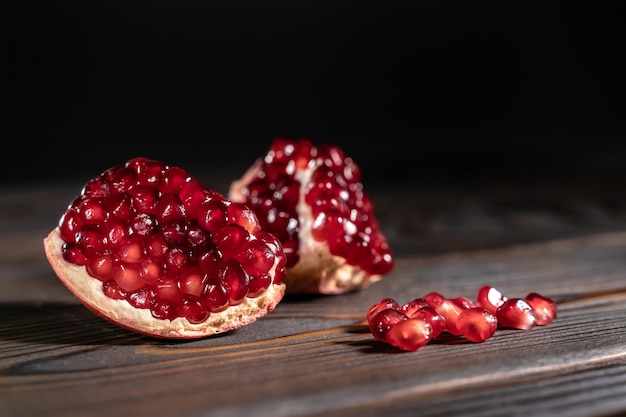 Craked ripe pomegranate and garnet seeds on dark wooden desk with place for text