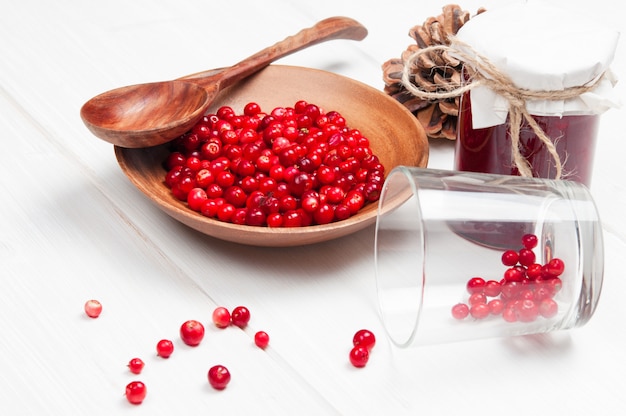 Cranberries in wooden bowl with spoon and jam in jar on white surface