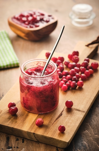 Cranberry jam in a glass jar on a wooden board.