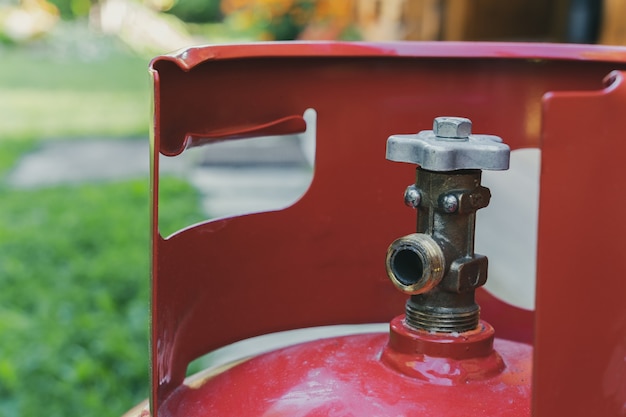 The crane of a portable and portable gas cylinder of red color close-up against the background of a garden with green grass.