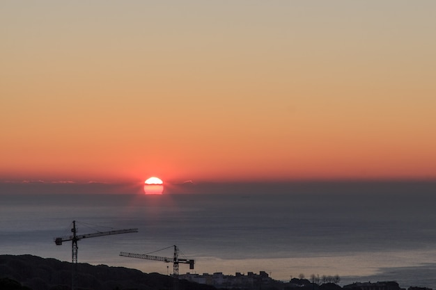 Cranes of works against the light with sunrise in the background