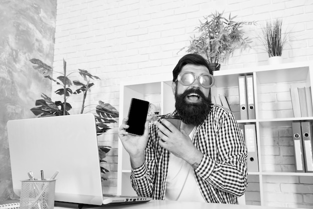 Crazy about technology Bearded man in funky glasses using smartphone with mobile technology New technology in modern office Taking advantage of mobile and online ordering technology