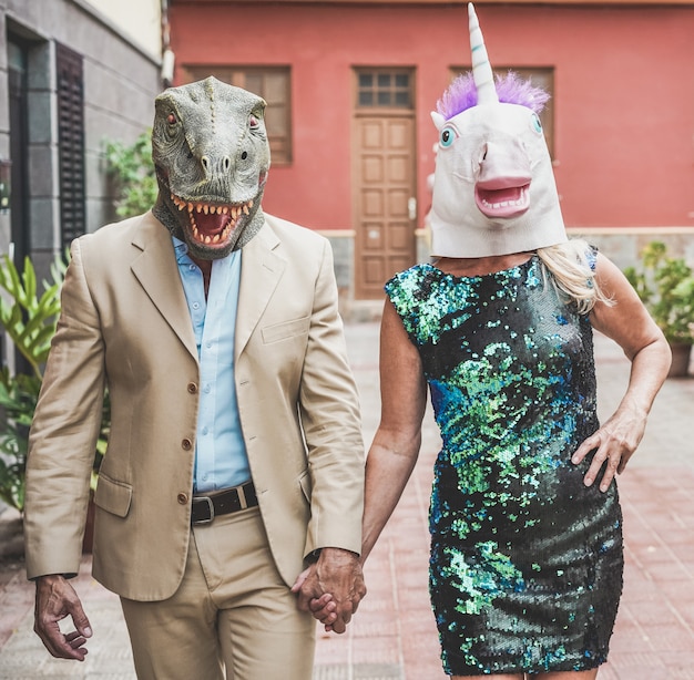 Crazy senior couple walking around city street wearing t-rex and chicken mask