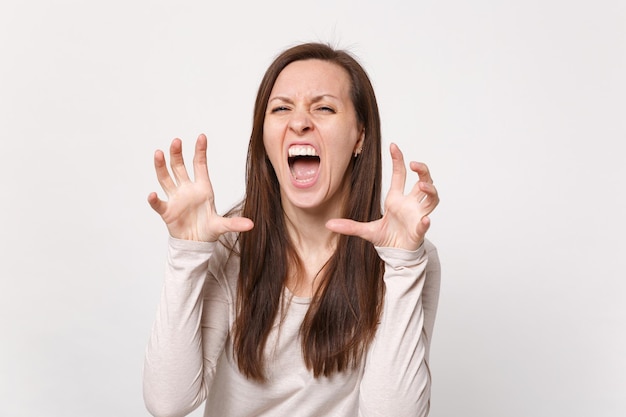 Crazy young woman in light clothes shouting, growling like animal, making cat claws gesture isolated on white wall background in studio. People sincere emotions, lifestyle concept. Mock up copy space.