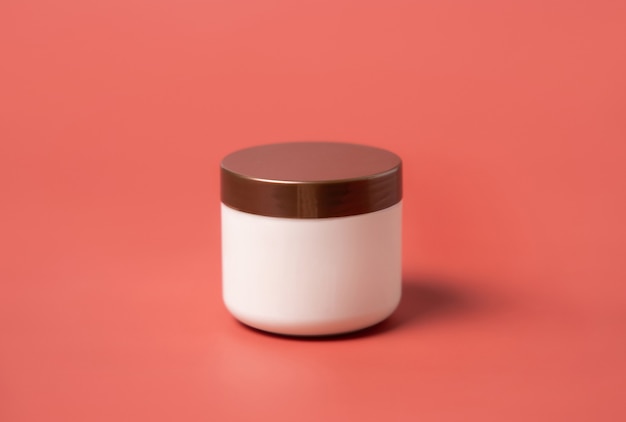 Cream blank jar with brown lid on pink background close up. Cosmetic cream can mockup