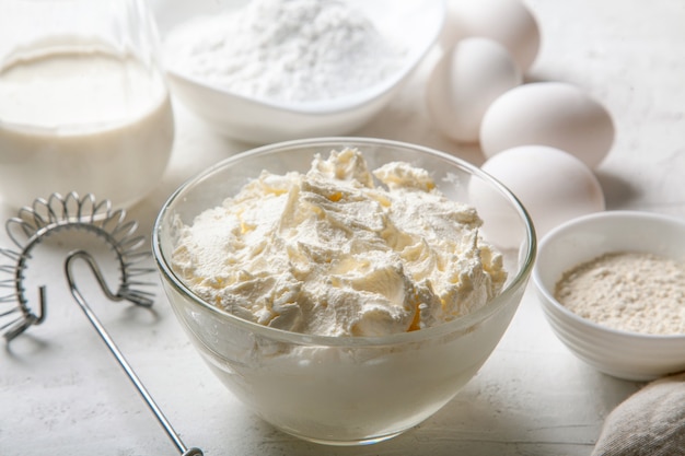 Cream cheese in glass bowl close up with sugar, eggs, flour and cream on light surface. Ingredients for cooking Basque Spanish burnt Saint Sebastian cheesecake. Recipe step by step.