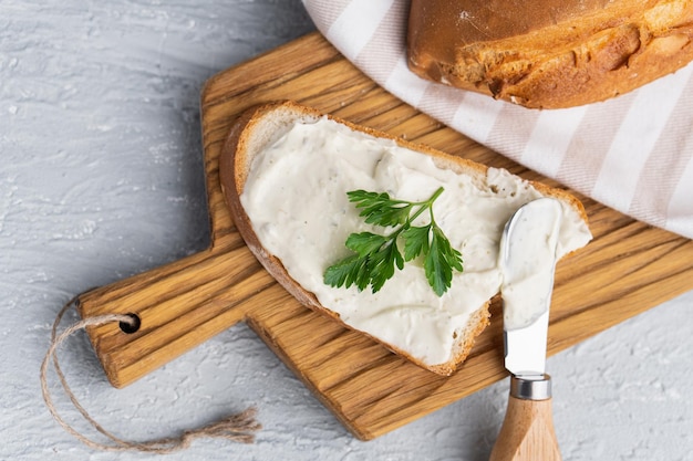 Cream cheese with herbs and seasoning on slice of fresh crunchy rye bread with cheese knife nearby