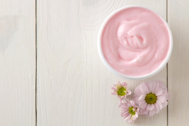 Cream cosmetics for face and body Pink cream and flower in a white jar on a white wooden table top view