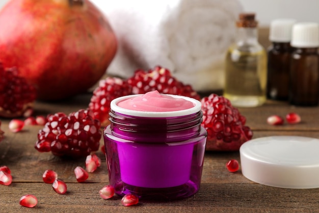 Cream cosmetics for face and body Pink cream and flowering branches and pomegranate in a purple jar on a brown wooden table