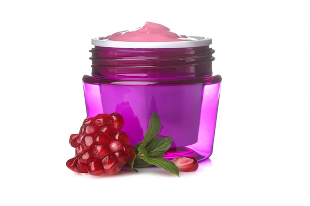 Cream in a jar next to fresh pomegranate on white isolated