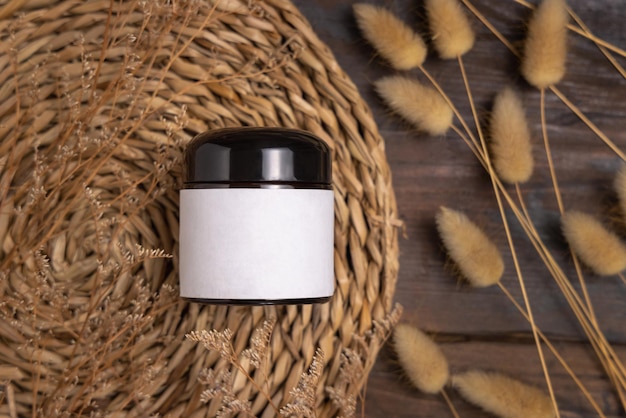 Cream jar with blank label on wattled placemat near Hare's Tail grass Cosmetic Mockup