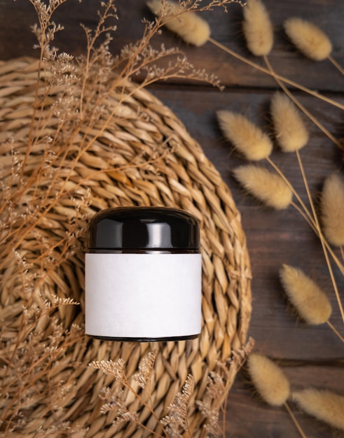 Cream jar with blank label on wattled placemat near Hare's Tail grass Cosmetic Mockup