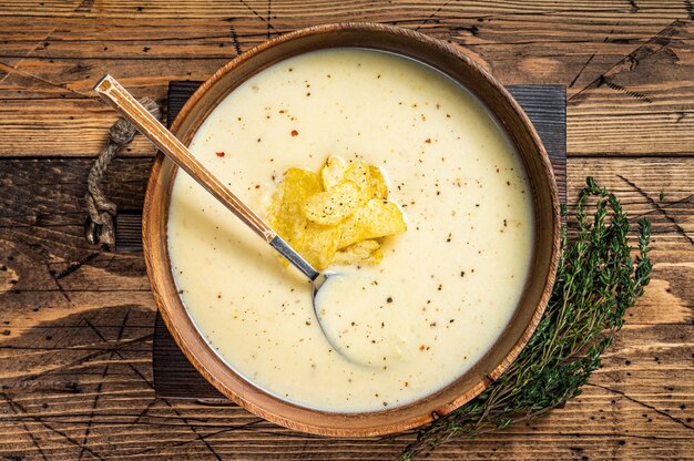 Photo cream potato soup with potato chips in wooden plate. wooden background. top view.