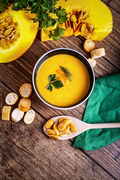 Cream pumpkin soup with fresh herbs and crackers on dark wooden background healthy food selective fo