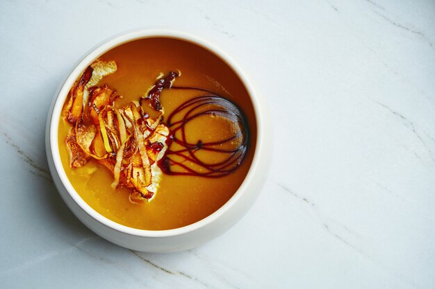 Cream soup orange color with dried wild mushrooms in a ceramic bowl on a marble surface. Vegetarian lunch. Top view, copy space