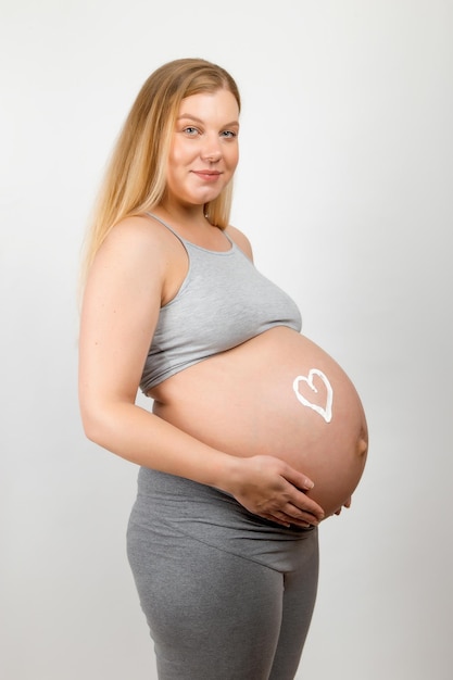 Cream on the stomach of a pregnant girl in the shape of heart Skin care for a pregnant woman