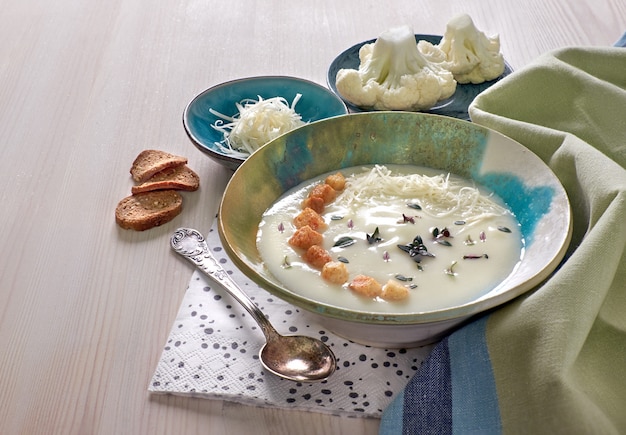 Creamy cauliflower soup in a blue cup with croutons and parmesan cheese