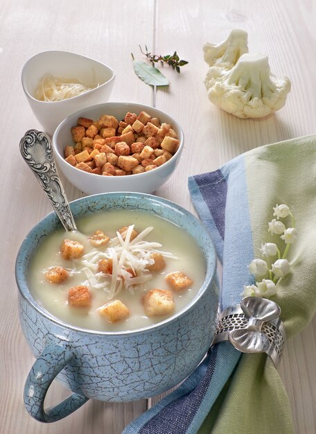 Creamy cauliflower soup in a blue cup with croutons and parmesan