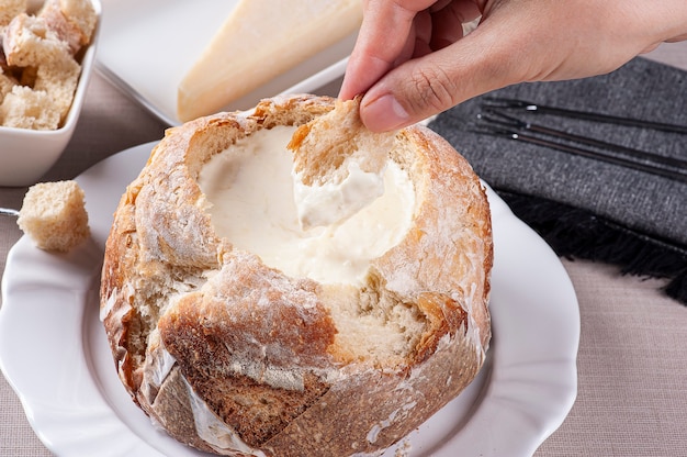 Creamy cheese fondue inside Italian bread and a hand dipping bread in it