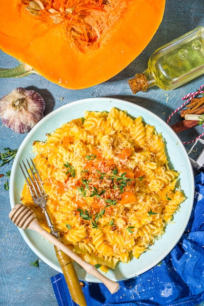 Creamy cheesy vegan pumpkin pasta, fusilli with pumpkin squash sauce, cheese and thyme, on concrete blue table background copy space