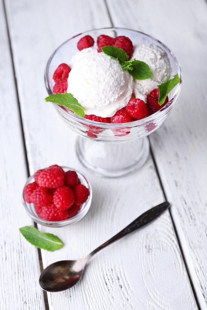 Creamy ice cream with raspberries on plate in glass bowl on color wooden background