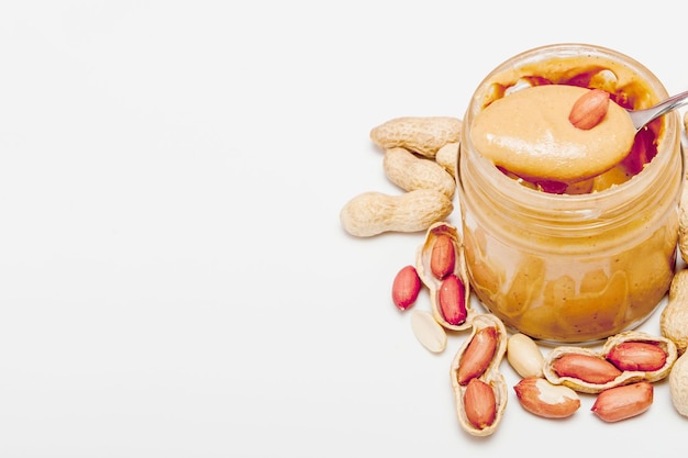 Creamy peanut butter in glass jar peanut and spoon isolated on white background A traditional product of American cuisine