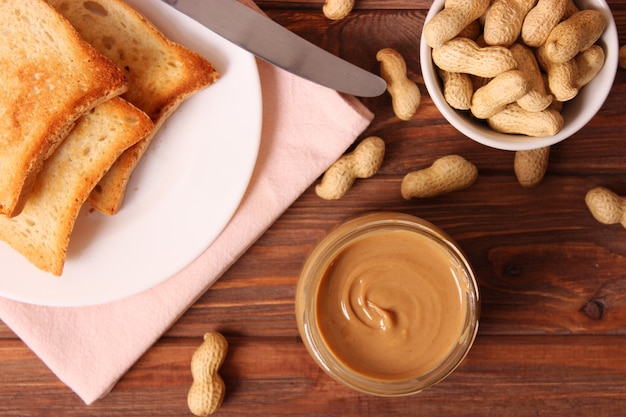 Creamy peanut butter and peanuts beans on wooden background top view