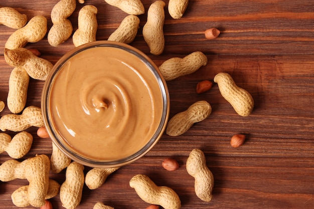 Creamy peanut butter and peanuts beans on wooden background top view