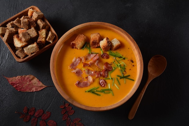 Creamy pumpkin and sweet potato (batata) soup with bacon on dark background.A bowl of the soup with homemade croutons and herbs with autumn decorations.