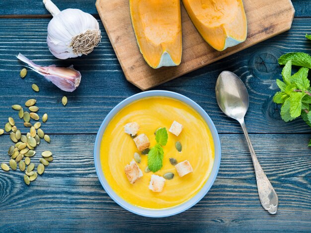 Creamy soup of pumpkin with croutons and seeds on dark blue wooden background