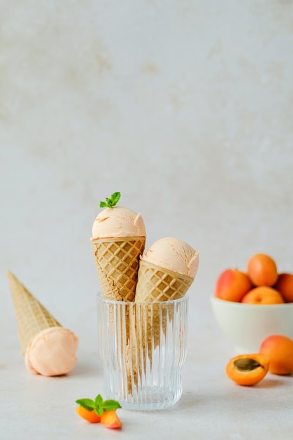 Photo creamy vegan apricot ice cream in the horn in a glass, styling mint leaves on top.