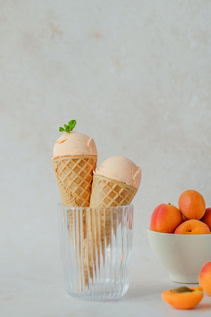 Creamy vegan apricot ice cream in the horn in a glass, styling mint leaves on top.