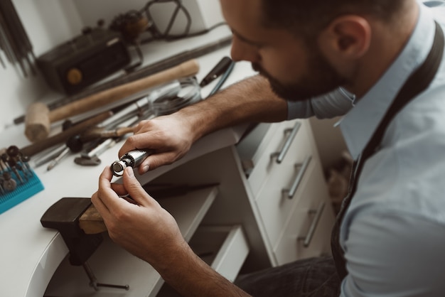 Creating art closeup photo of male jeweler making a new silver ring at his workbench