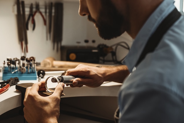 Creating a beauty. Close-up portrait of bearded male jeweler polishing a detail. Jewelry manufacturing concept.