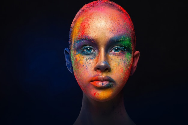 Photo creative art make up. holi colors. portrait of young fashion model with bright colorful mix of paint on her face.