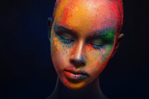 Photo creative art make up. holi colors. portrait of young fashion model with bright colorful mix of paint on her face.