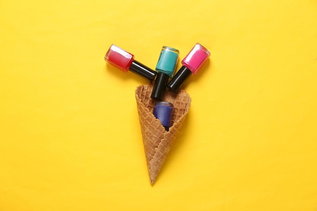 Creative beauty layout Waffle cone with nail polish bottles on yellow background Flat lay